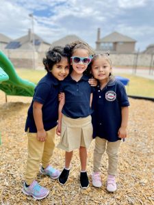 Three cheerful children smiling and posing together outdoors on the playground at Pinnacle Montessori of Castle Hills.