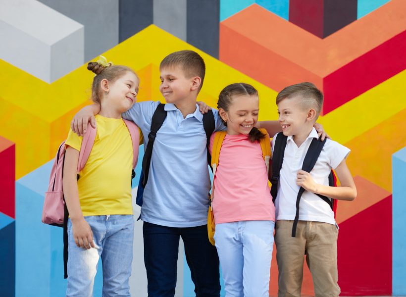 Happy schoolkids hugging near a colorful wall.